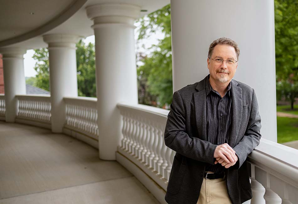 Daniel Schwabauer, assistant professor of English, leaning on the balcony railing of the Cunningham Center over looking the campus mall.