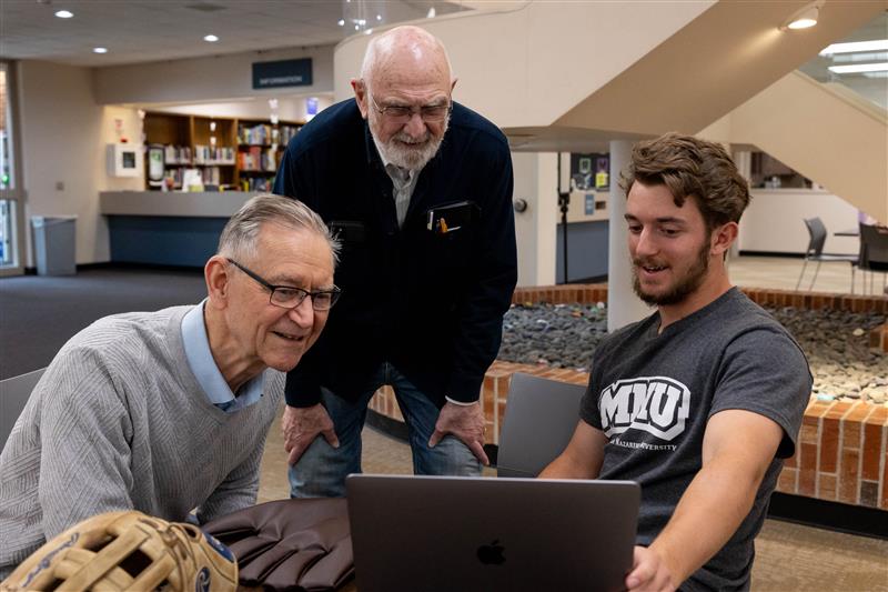 Two older gentlemen look at laptop with MNU history student