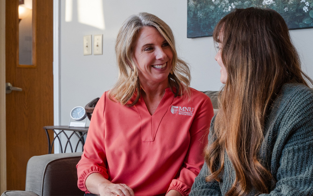 A counselor and participant sitting on a sofa speaking to one another.