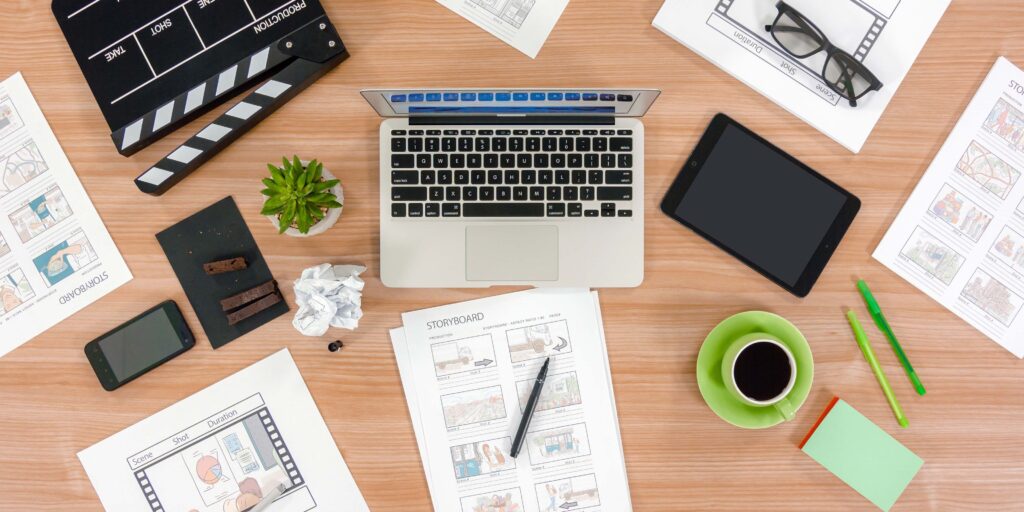 laptop on a desk surrounded by paper, pens, coffee mug, table and phone.