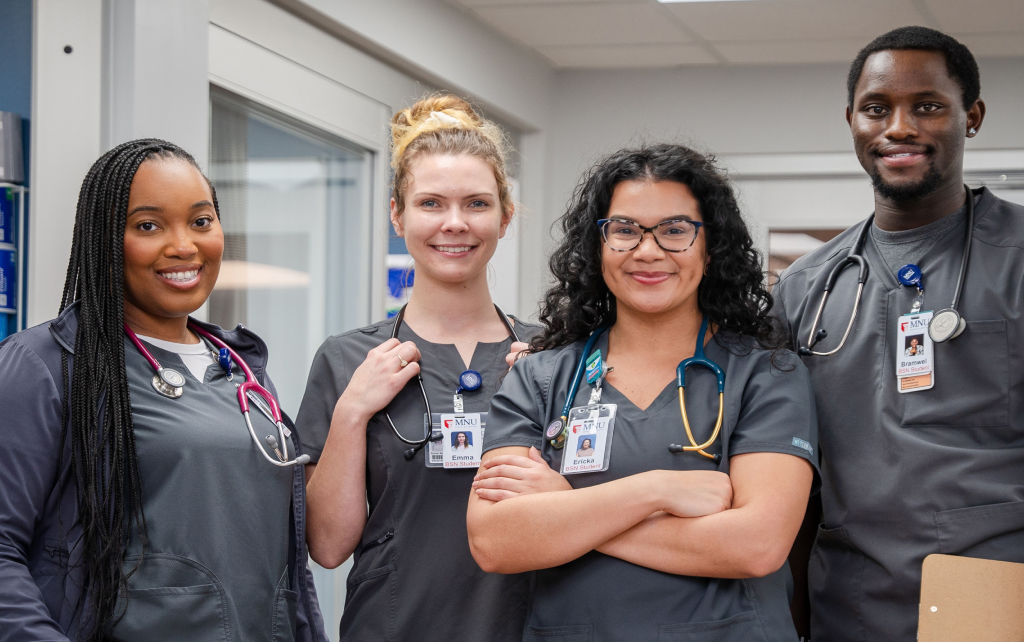 A group of four nursing students standing together in a nursing lab