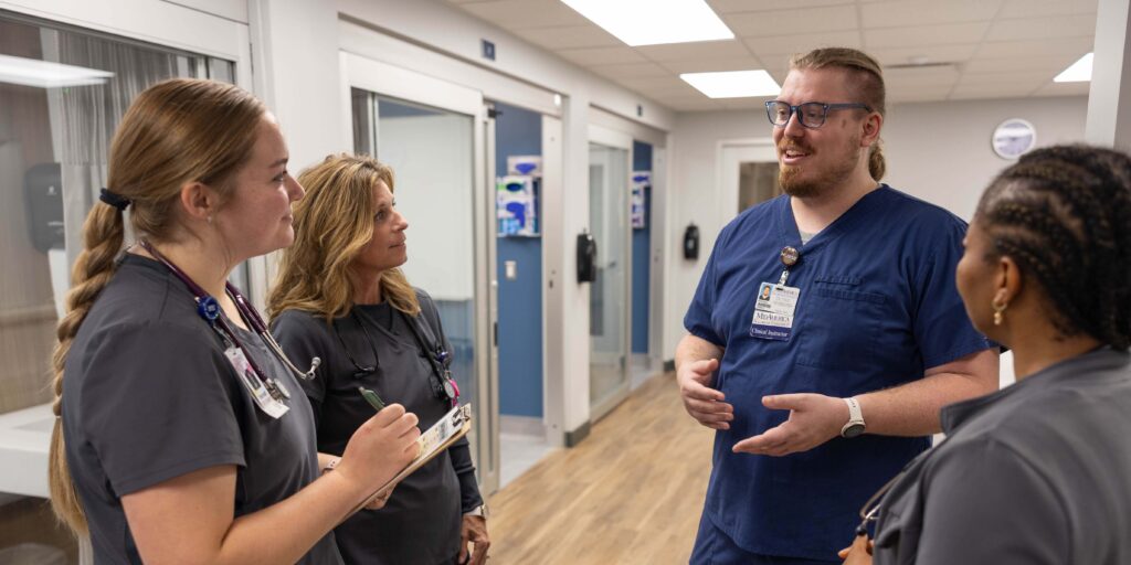 Jared Kellum in MNU SIM lab talking with three female students.