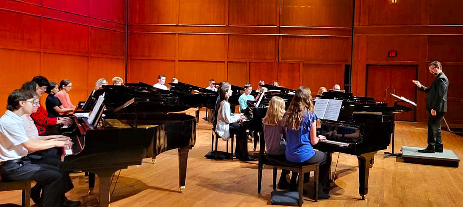 A concert stage with several grand pianos and pianists all playing