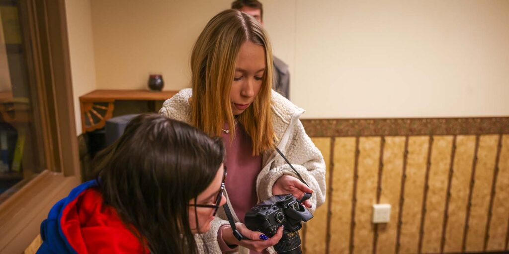 Two students with camera at staged crime scene in lab.