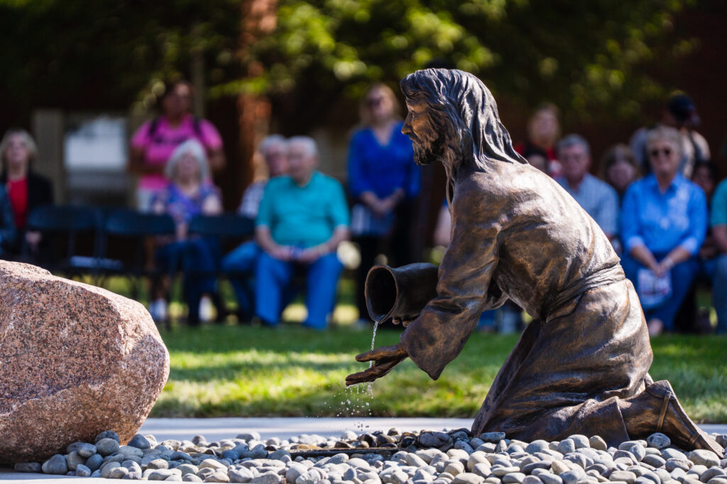 Dedication ceremony of the Purposeful Life statue on MNU's campus, featuring a statue of Jesus kneeling with a pitcher of water in front of a rock
