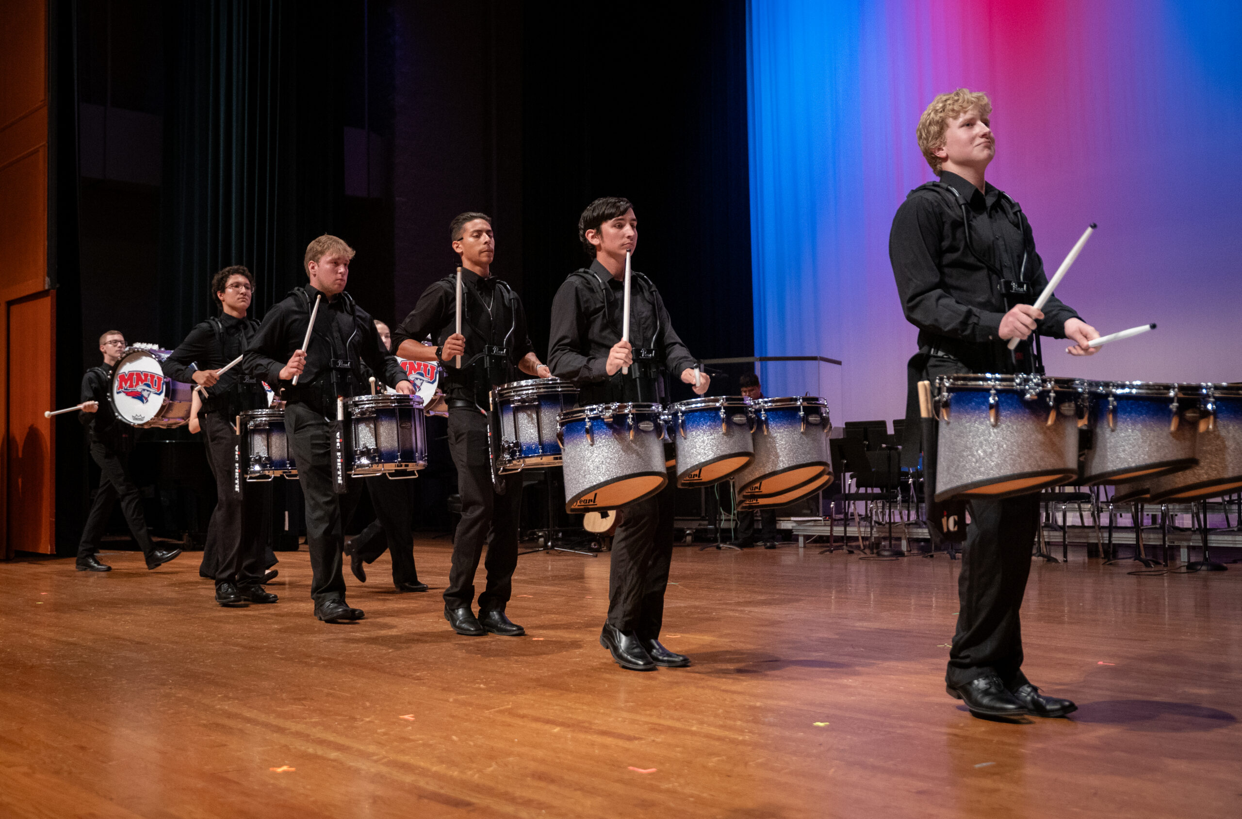 Drumline players perform on stage, standing in formation